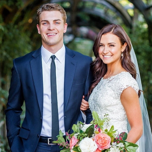 Wedding couple smiling outdoors with flowers and greenery.