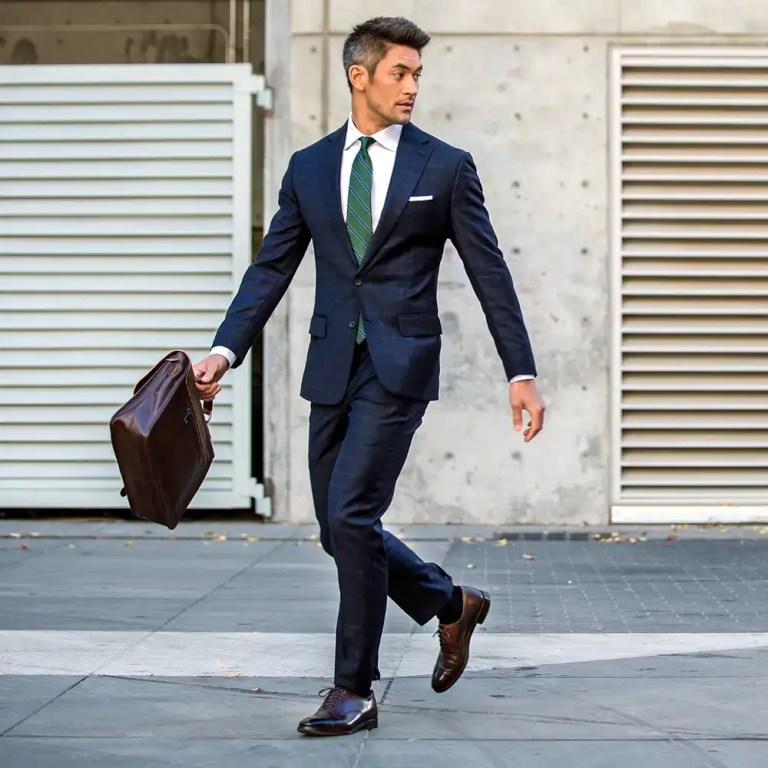 Business professional in a navy suit walking with a briefcase in a city environment.
