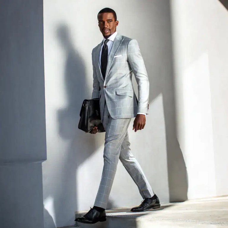 Man in stylish gray checkered suit with black shoes and briefcase.