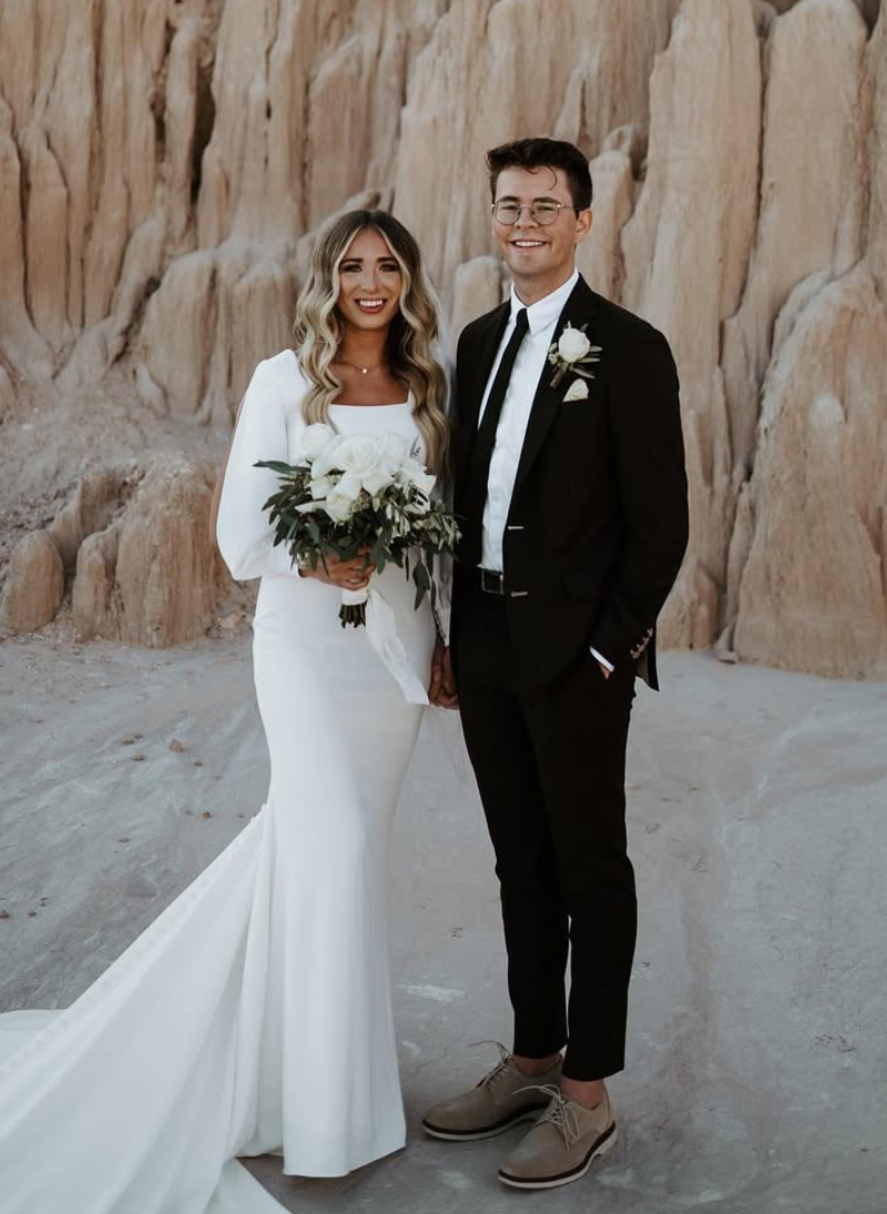 Bride and groom smiling in wedding attire against a rocky desert backdrop.