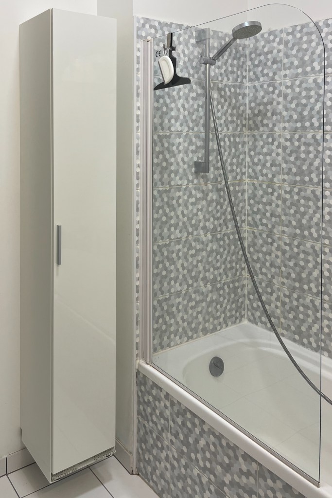 Slim white bathroom cabinet next to shower