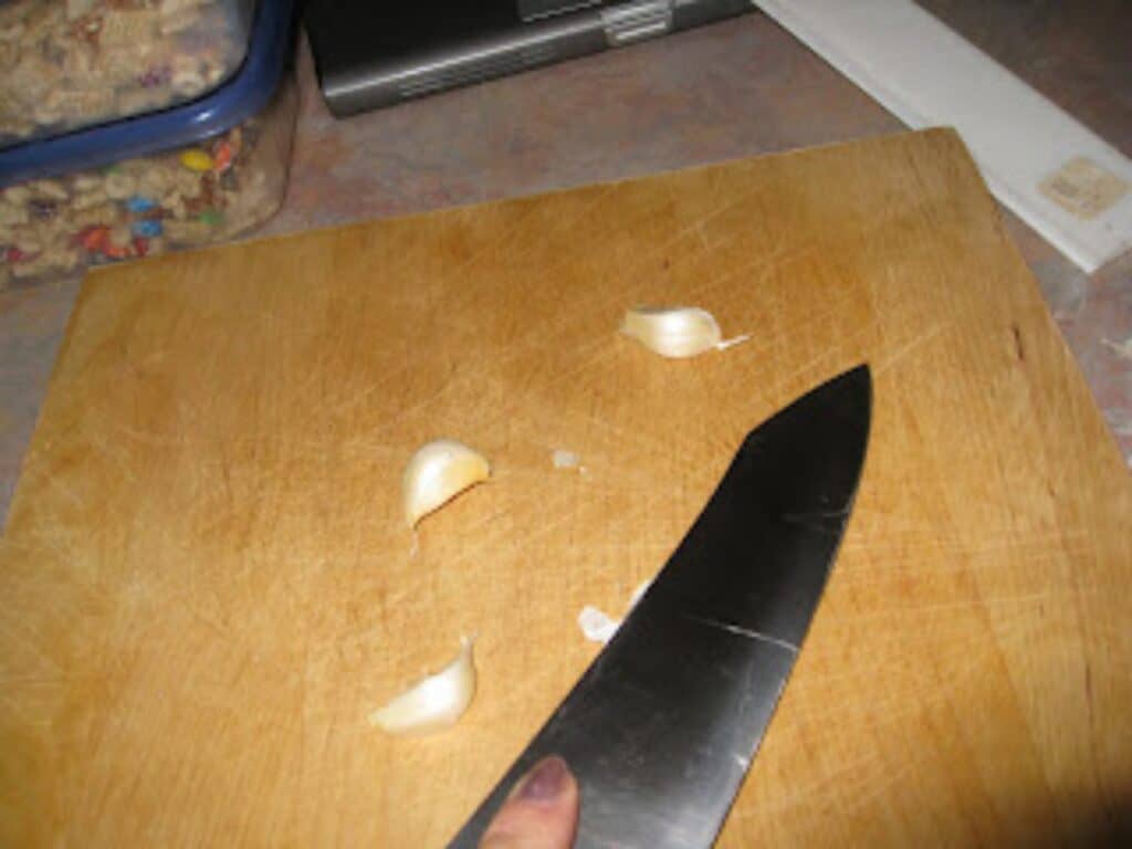 Image shows garlic on chopping board.