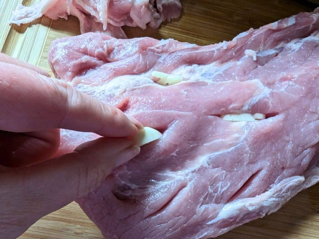 Adding sliced garlic to pork.