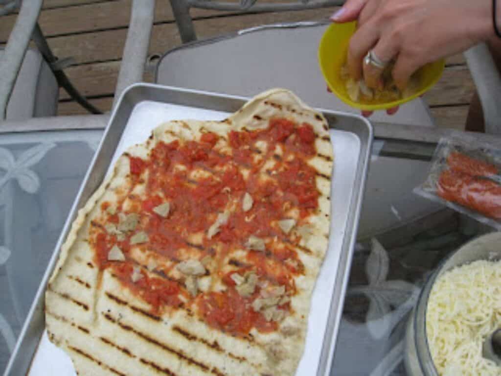Image shows grilled pizza dough with toppings.