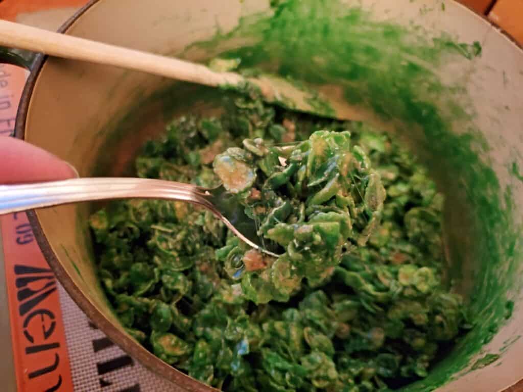Spoon holding a serving of green marshmallow covered corn flakes.
