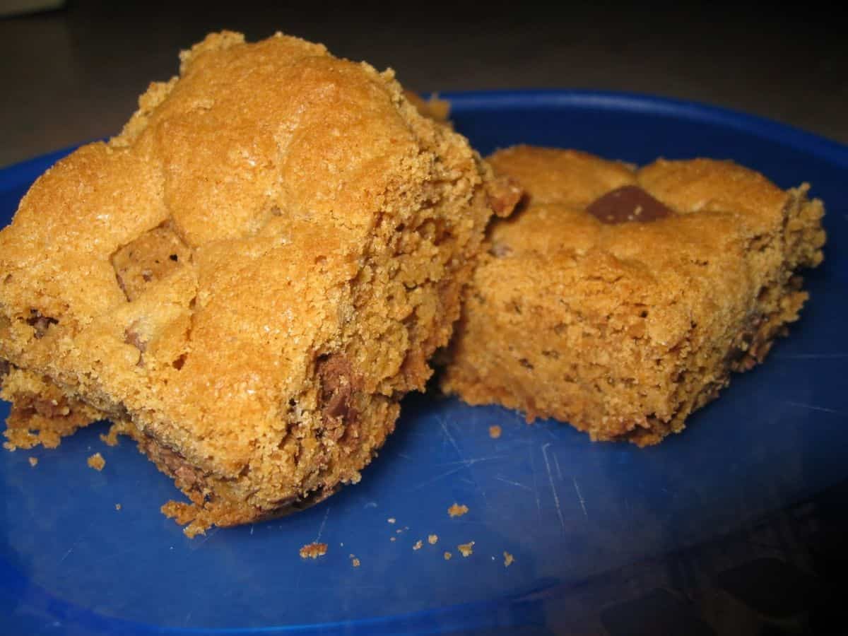 Two square pieces of golden-brown cookie bars with visible chocolate chunks, served on a blue plate.