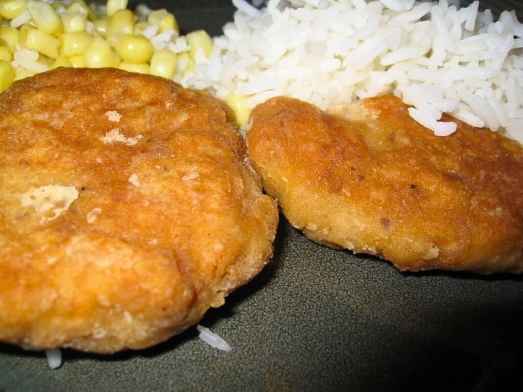 Image shows two salmon patties on a green plate served with rice and corn.