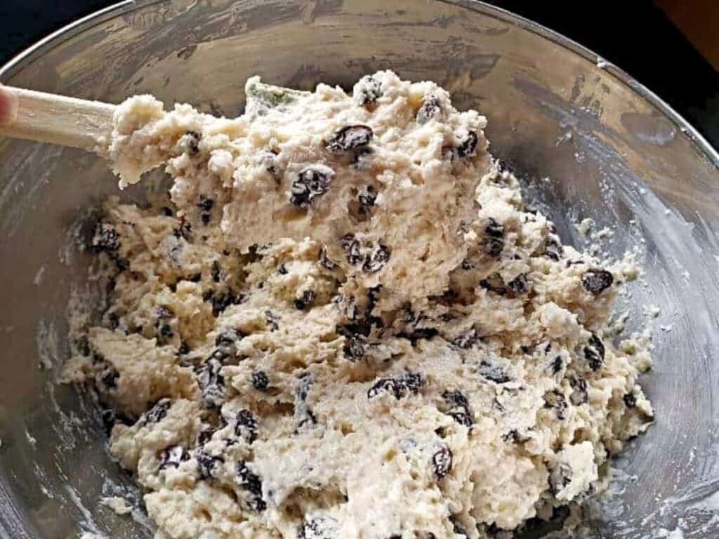 Cookie dough with raisins being mixed in a metal bowl with a wooden spoon.