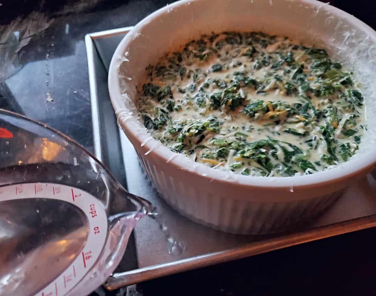 Pouring water in a baking pan for a water bath with a spinach souffle.