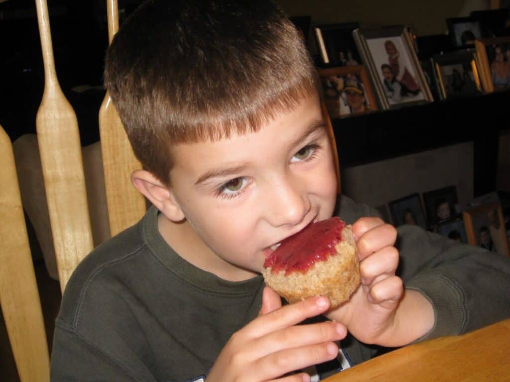 Image shows little boy holding and eating strawberry cupcake with cherry glaze.