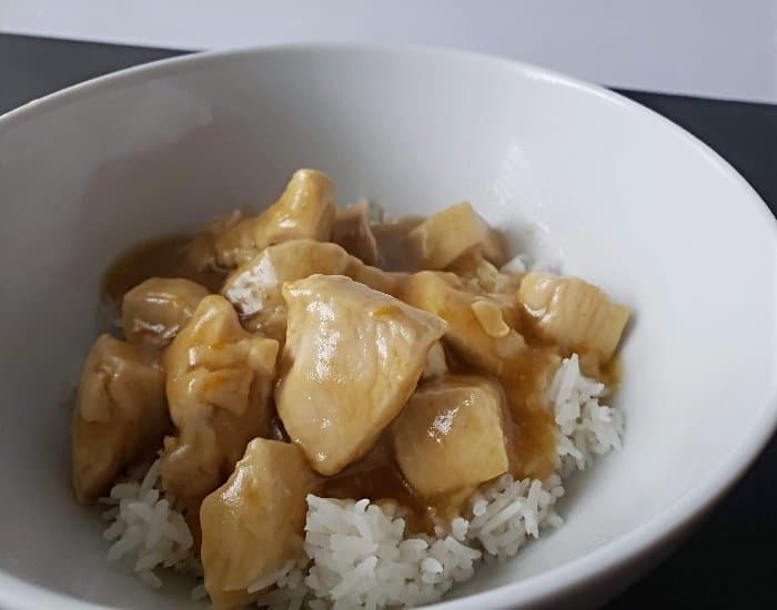 Image shows a Fork holding orange chicken with rice with the full bowl behind it.