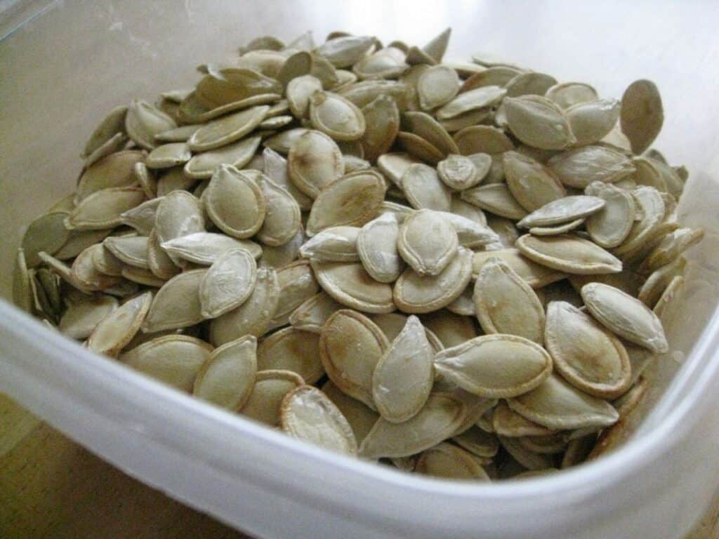 Image shows roasted pumpkin seeds in a food storage container.