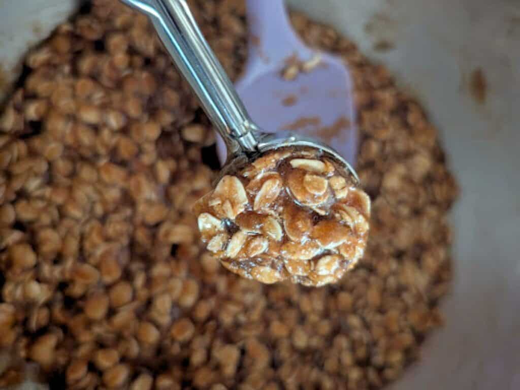 A metal scoop holds a portion of oat and peanut butter mixture above a bowl filled with the same—perfect for making crisp, lacy cookies.