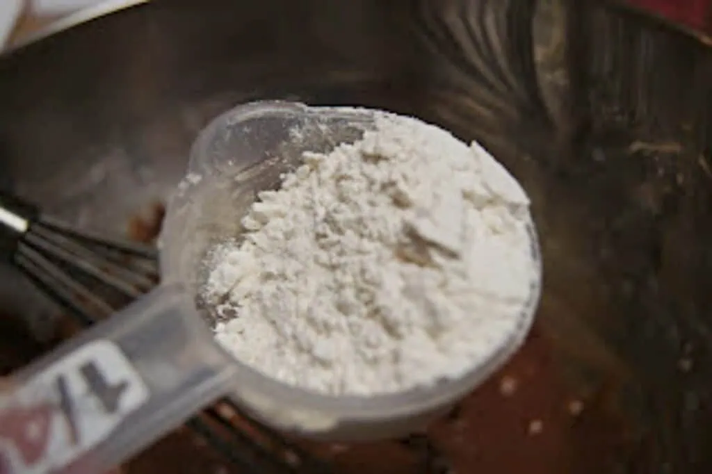 Scant quarter cup of flour held over a bowl of chocolate batter.