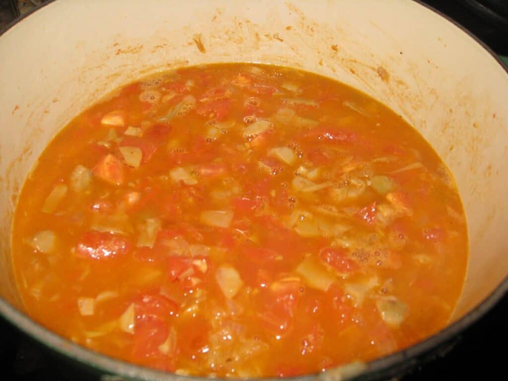 Image shows vegetables with stock added in a saucepan.