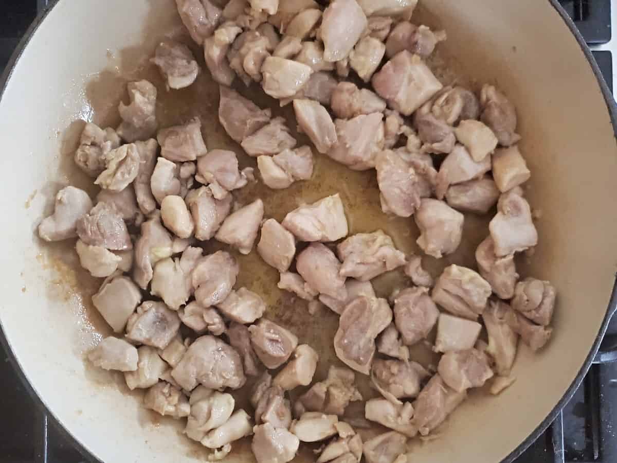 Chicken thigh pieces sauteeing in an enameled cast iron skillet.