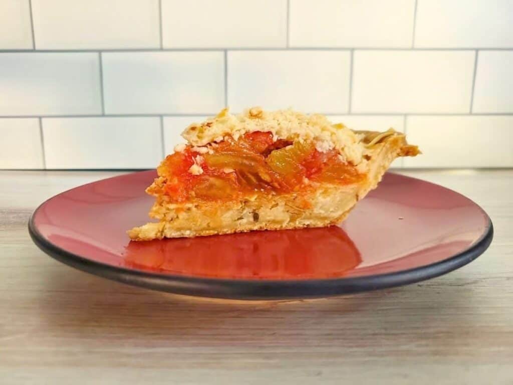 A slice of fruit pie with a crumb topping on a red plate.