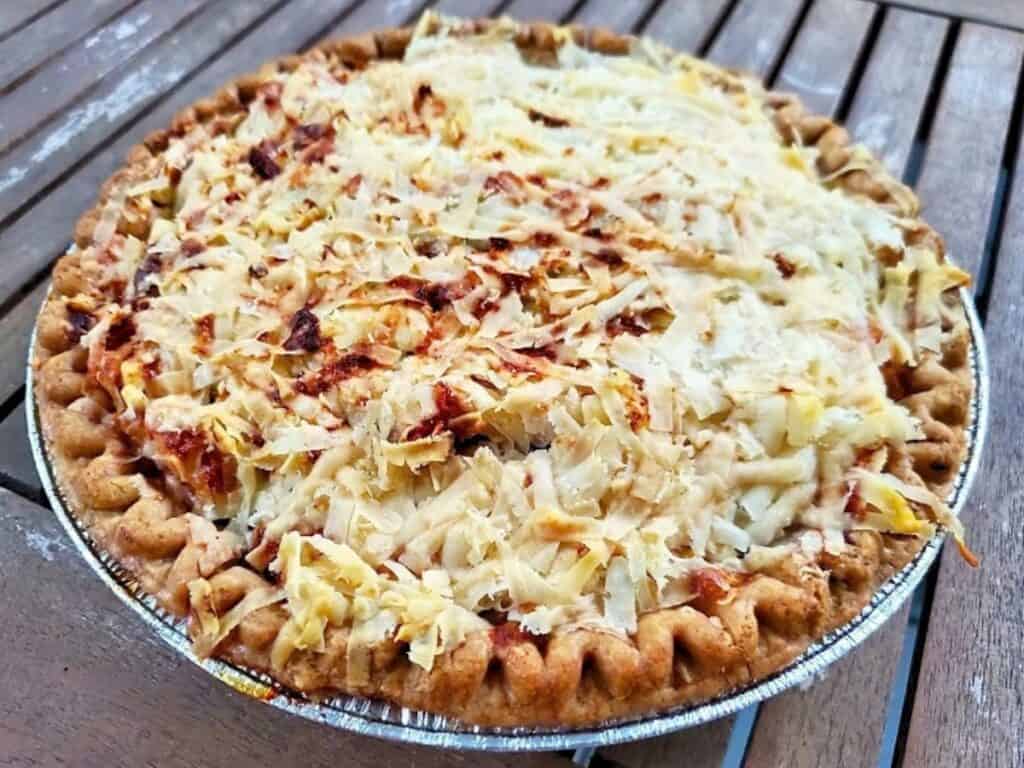 A savory pie in a foil tin topped with a generous layer of shredded cheese.