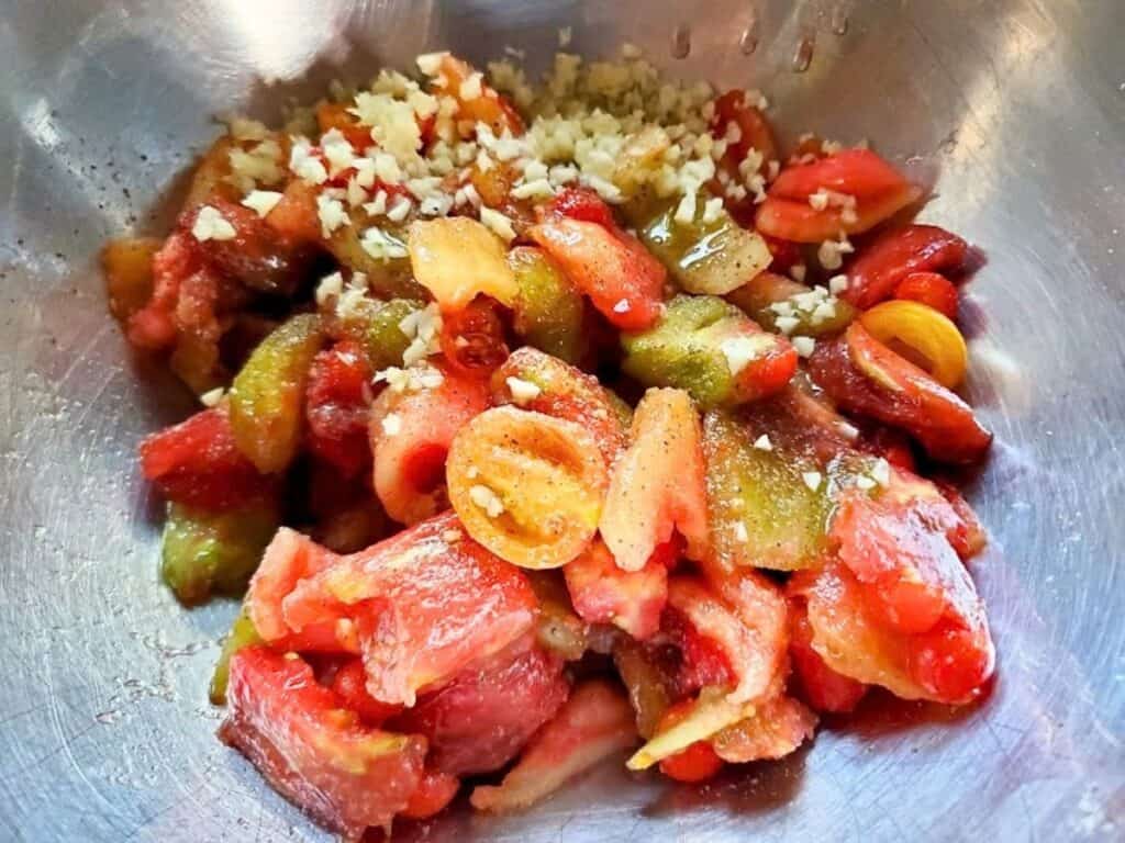 Chopped tomatoes and minced garlic in a stainless steel bowl.