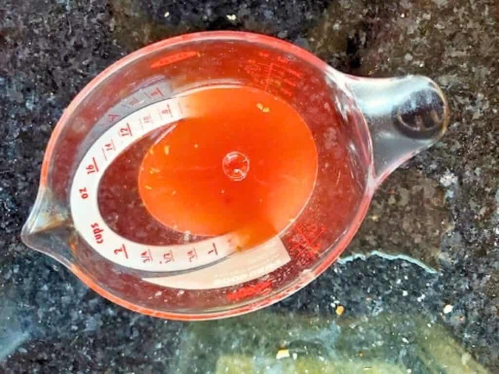 A glass measuring cup containing approximately one cup of orange-red liquid on a dark countertop.