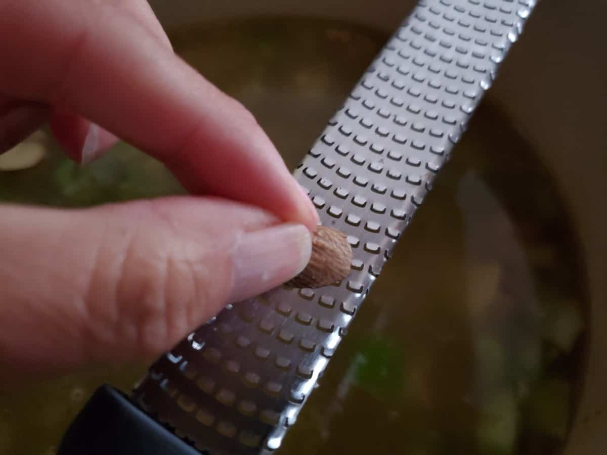 Grating nutmeg into a pot of soup.