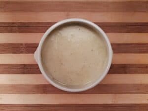 Overhead view of a bowl of homemade cream of celery soup on a wooden board.