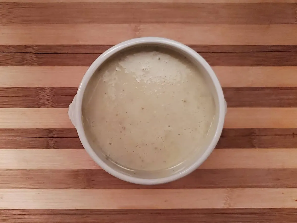 Overhead view of a bowl of homemade cream of celery soup on a wooden board.