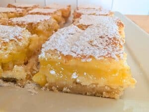 Close-up of lemon bars on a plate, featuring a crumbly crust, vibrant baked lemonade filling, and a dusting of powdered sugar on top.