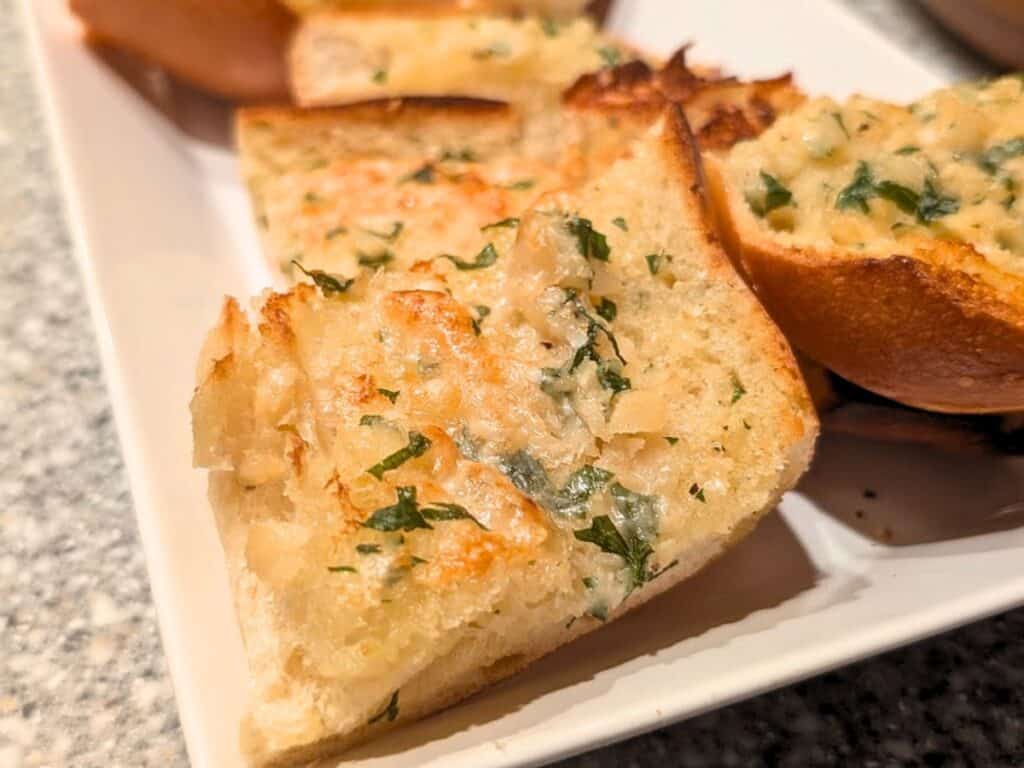 Slices of garlic bread with chopped parsley and melted butter on a white plate.