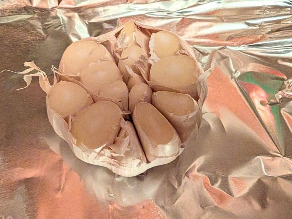 A head of garlic with the top cut off, exposing the cloves, sits on a sheet of aluminum foil.