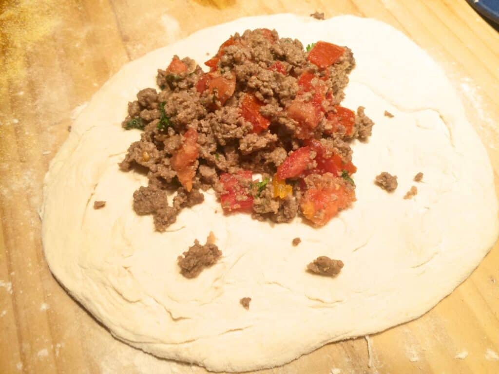 Image shows placing meat filling on dough.
