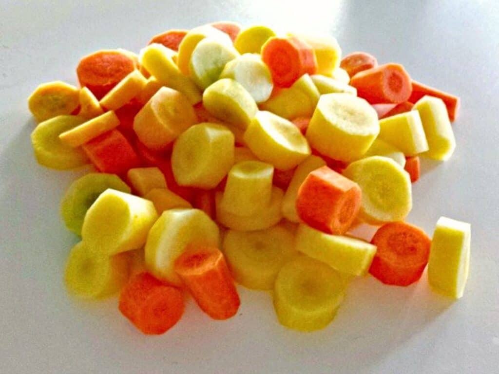A pile of sliced orange, yellow, and white carrots on a white surface.