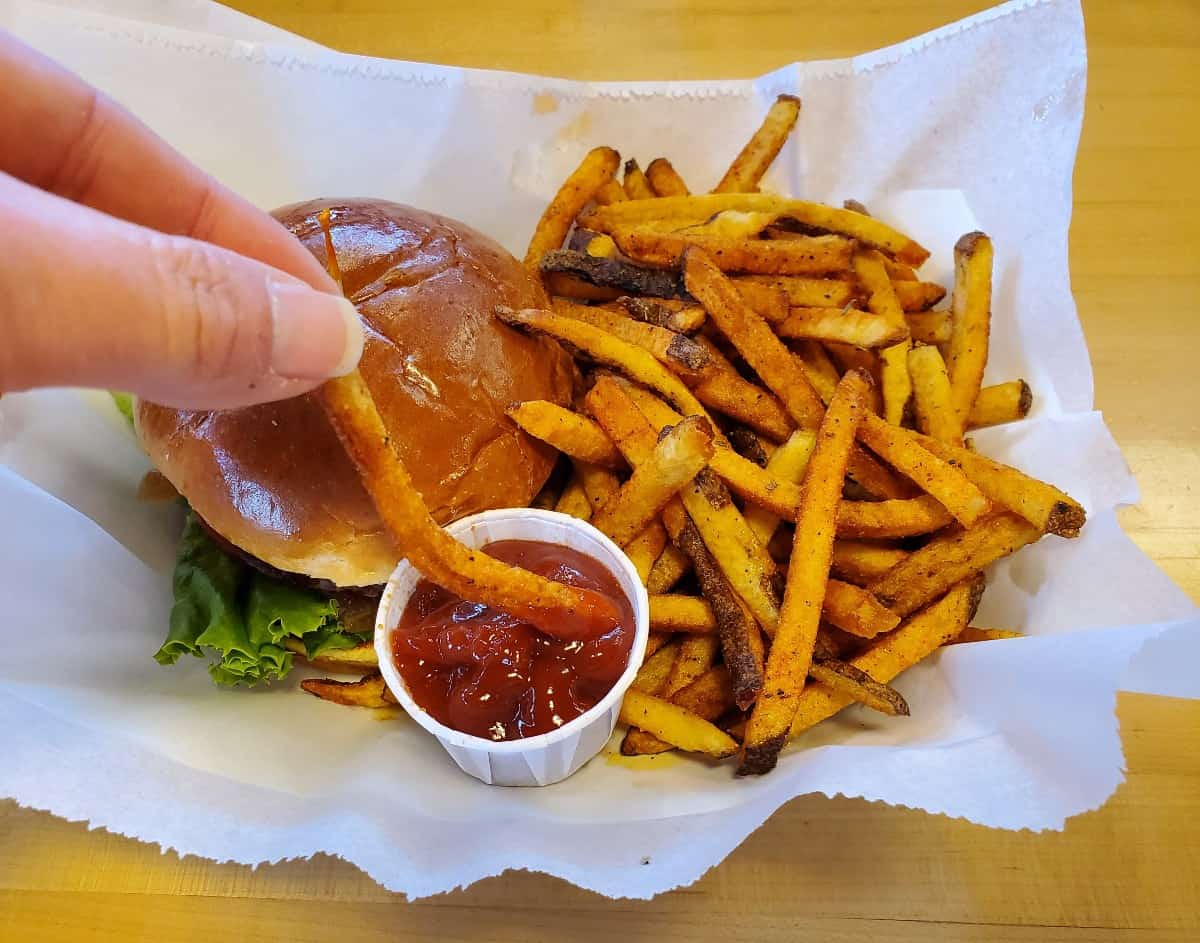 Dipping a french fry in ketchup that's sitting in a burger basket.