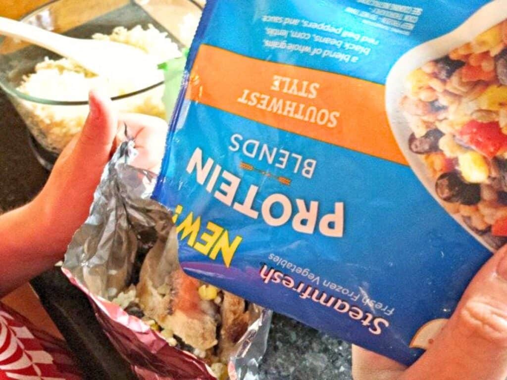 A person pours a bag of Southwest Style protein blend vegetables into a silver container, with a bowl of grilled chicken pockets visible in the background.