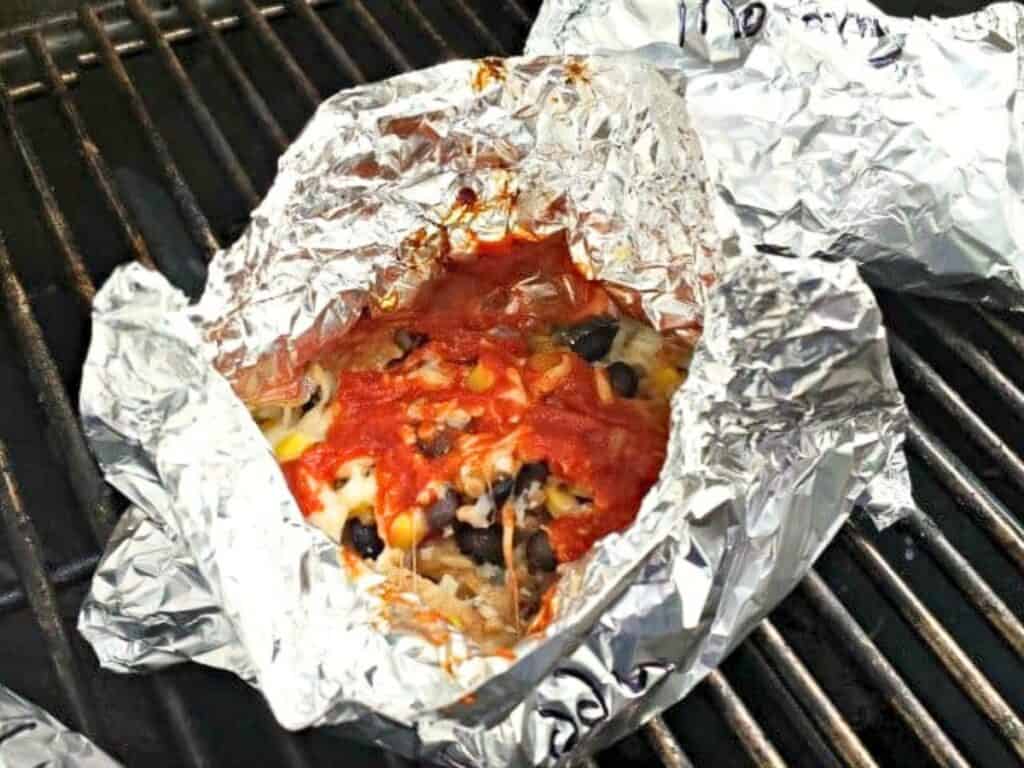 Foil packet open on a grill, showing a mixture of red sauce, melted cheese, onions, and black beans inside—perfect for making delicious grilled chicken pockets.