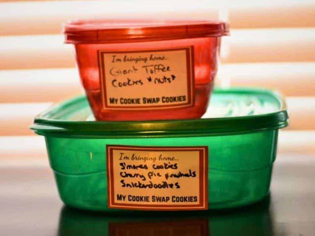 Two plastic containers labeled “My Cookie Swap Cookies,” one red and one green, list cookies inside, including giant toffee cookies with nuts, irresistible s’mores cookies, cherry pie pinwheels, and classic snickerdoodles.