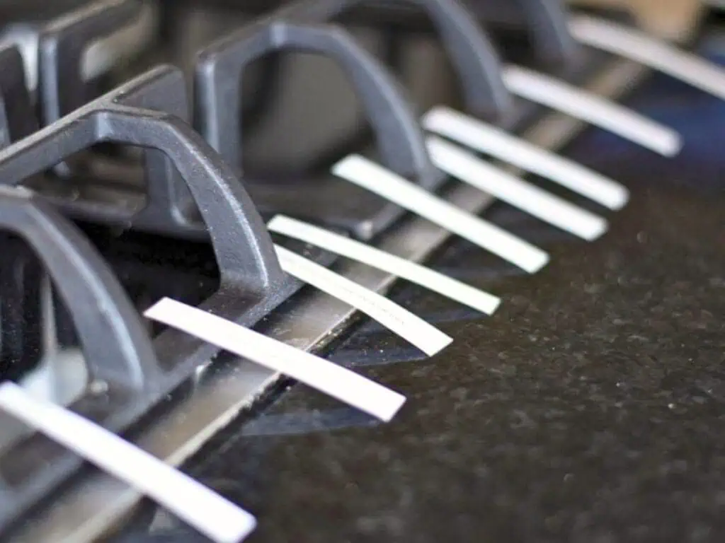 Several white strips of paper are evenly spaced and laid across the grates of a black gas stove and the adjacent countertop.