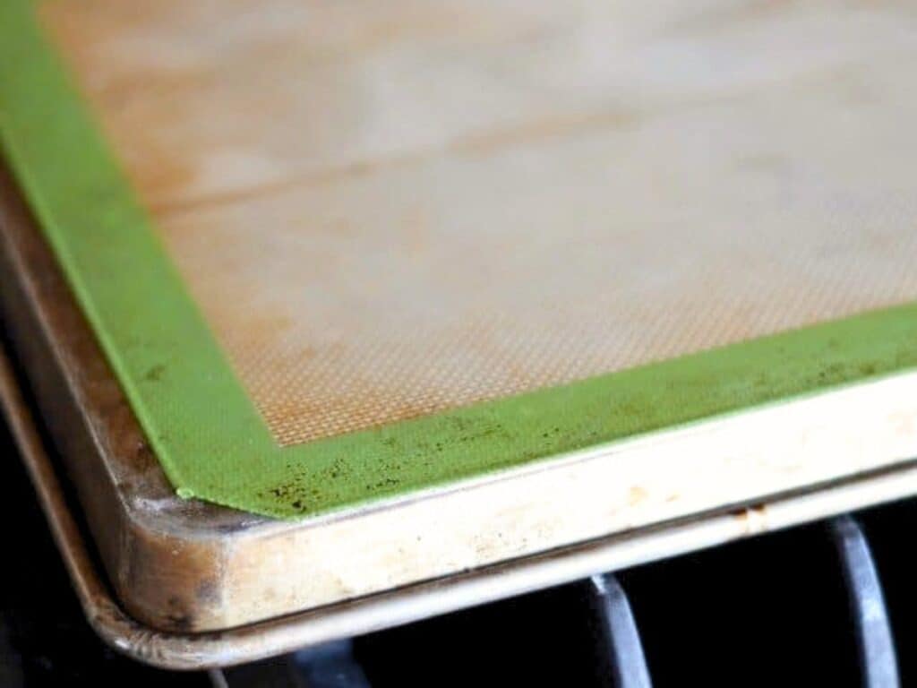 A close-up of a baking sheet lined with a silicone baking mat featuring a green border, placed on an oven rack.