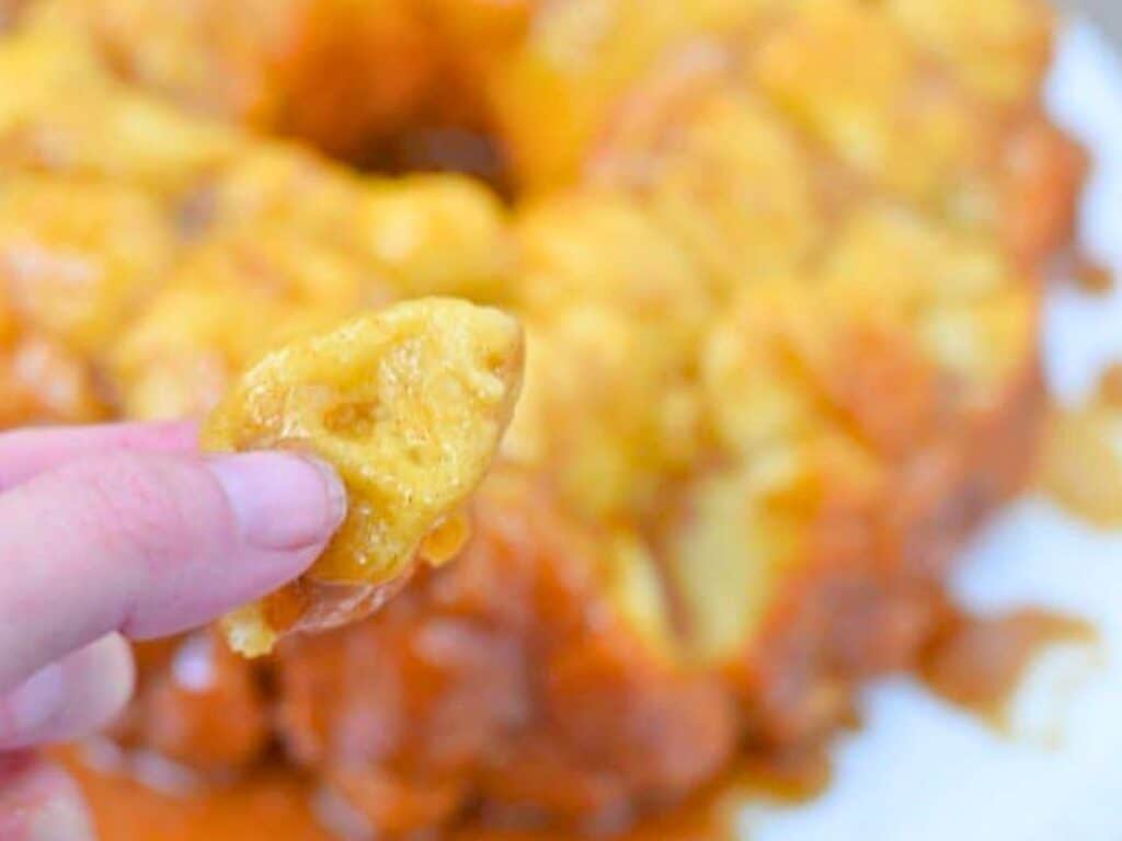 A hand holding a piece of cheesy, pull-apart bread with more bread and melted cheese visible in the background.