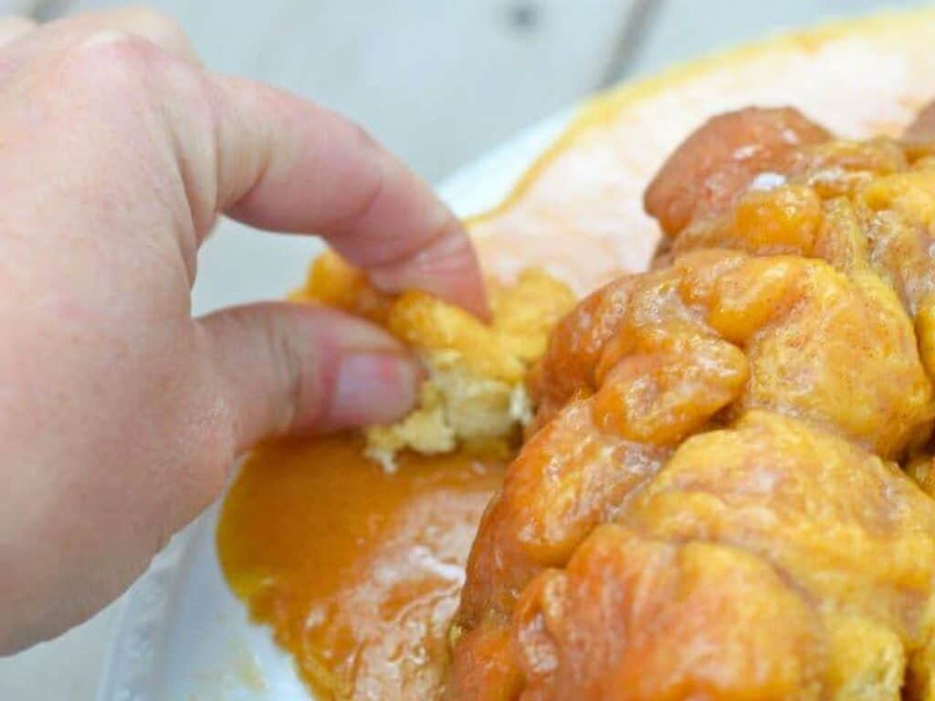 A hand pulling a piece from a plate of sticky, glazed monkey bread.