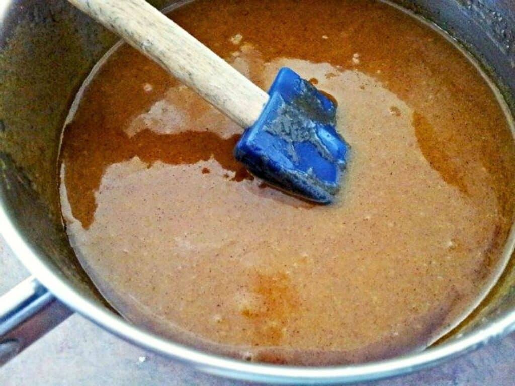 A saucepan filled with a thick brown mixture being stirred with a blue spatula.