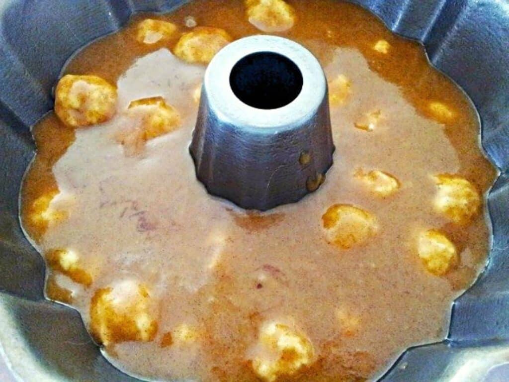Bundt pan filled with light brown cake batter, showing unevenly distributed lumps, ready to be baked.
