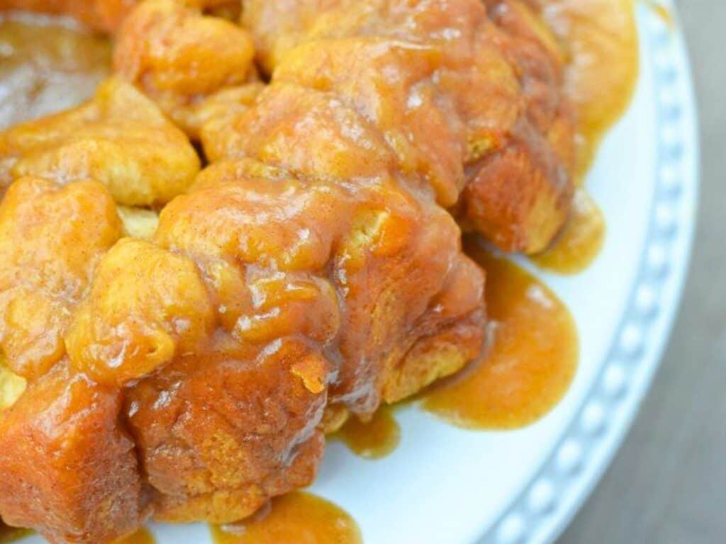 Close-up of golden-brown monkey bread with caramel glaze, served on a white plate with a dotted rim.
