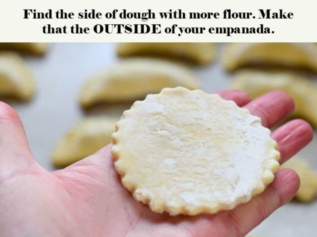 A hand holds a round, floured dough disc with empanadas in the blurred background. Text above gives instructions for making empanadas.