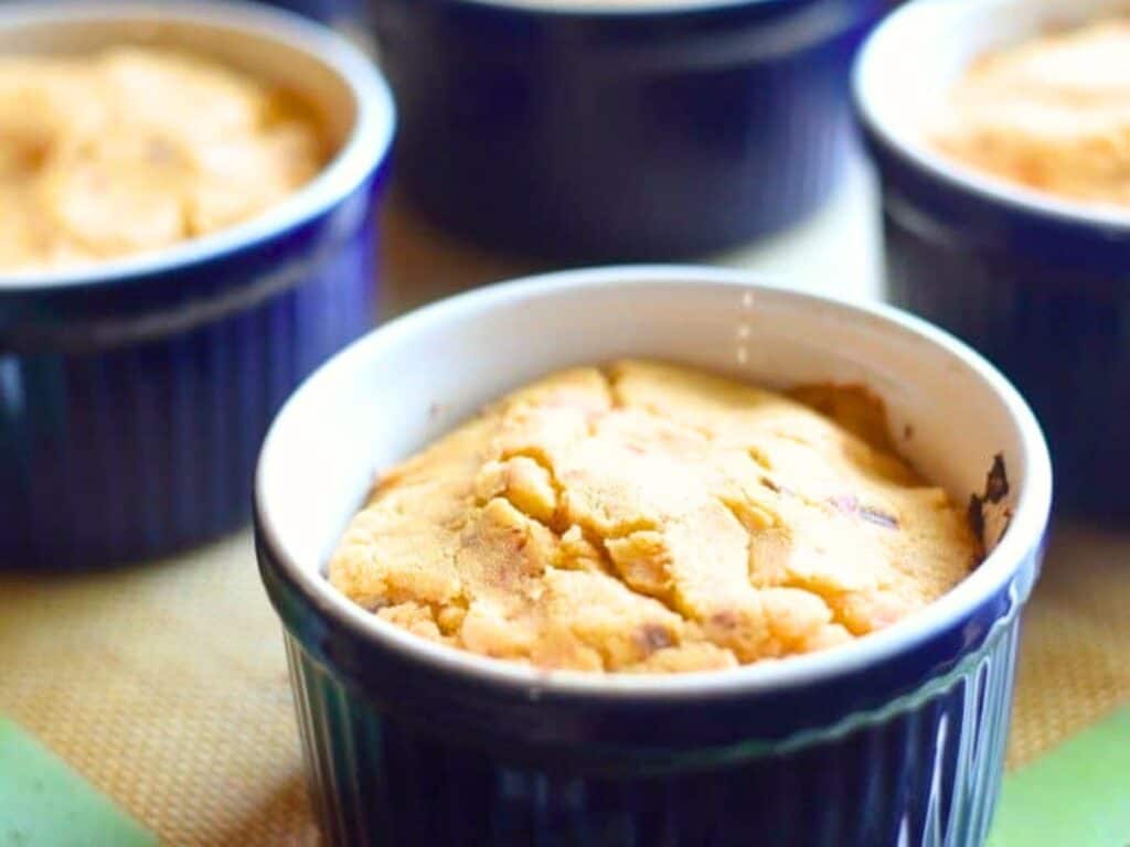 Four blue ramekins filled with freshly baked, golden brown tamale pot pie cornbread muffins sit on a table.