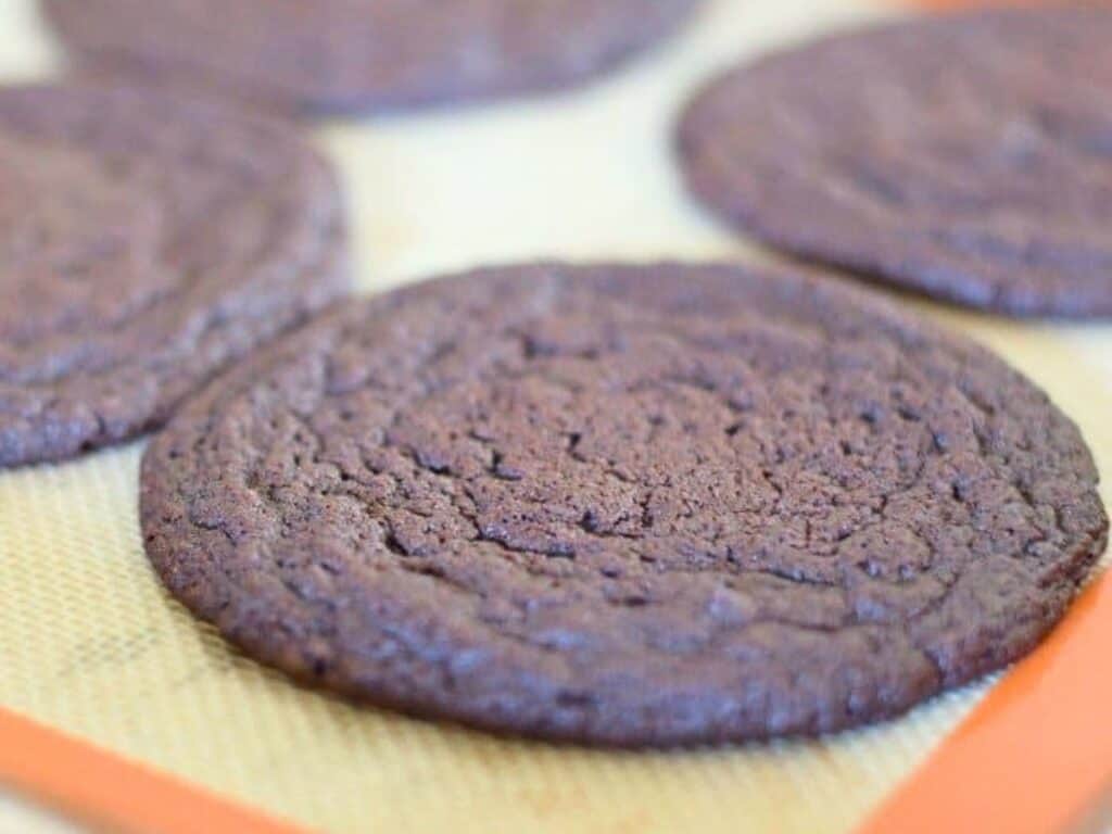 Close-up of several large, round chocolate cookies on a silicone baking mat.