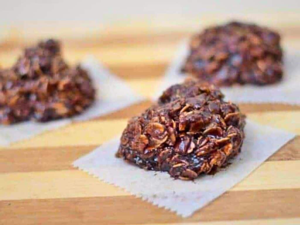 Three Nutella no bake cookies sit on individual parchment paper squares atop a wooden surface.