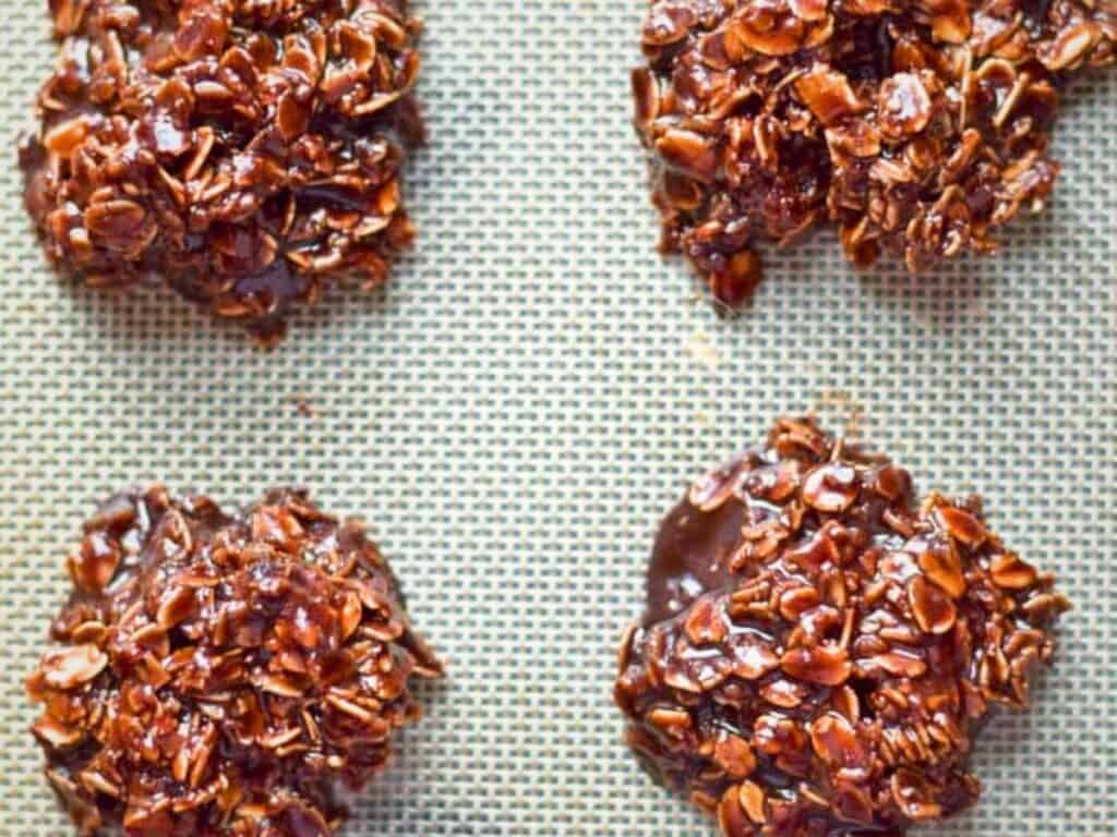 Four chocolate oatmeal nutella no bake cookies are arranged on a silicone baking mat, spaced apart in a grid pattern.