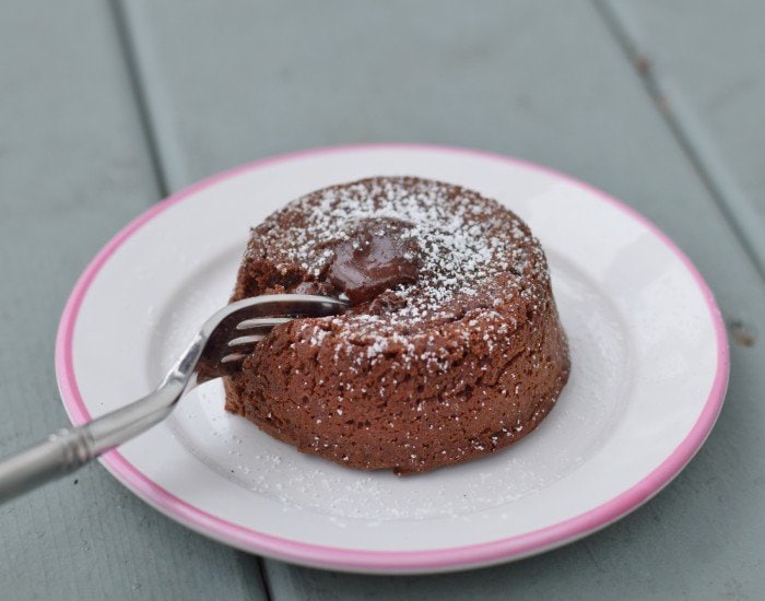Fork cutting into a molten chocolate cake on a small white plate.