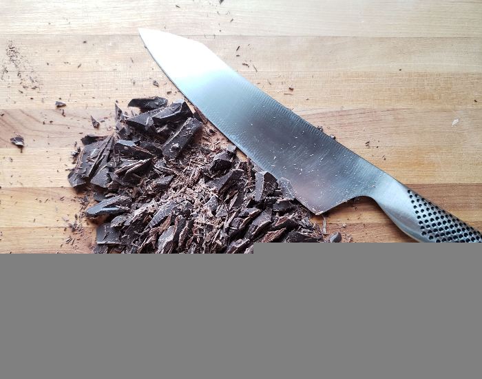 Chopped chocolate on a wooden cutting board with a knife next to it.